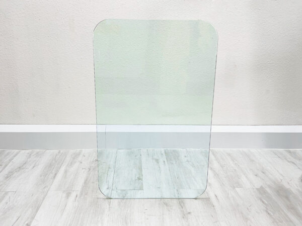 Aufrechtstehende, rechteckige, durchsichtige Glas Tischplatte mit abgerundeten Kanten auf weißem Holzboden vor weißem Hintergrund