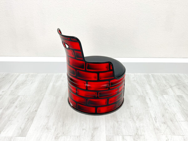 Oelfass Sessel Frieda halb von hinten fotografiert in roter Grundfarbe mit aufgesprayten Backsteinen, schwarzem Sitzpolster, schwarzem Kantenschutz und Stauraum unter der Sitzflaeche vor weißem Hintergrund