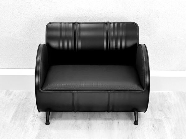 Frontalansicht von schwarzem Oelfass Sofa mit schwarzer Polsterung auf weißem Holzboden vor weißer Wand