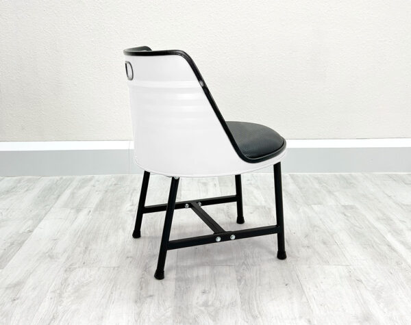 Seitliche Ansicht von Esszimmer Stuhl aus Oelfass mit schwarzem Sitzpolster, schwarzen Metallbeinen und schwarzem Kantenschutz auf weißem Holzboden vor weißem Hintergrund