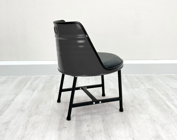 Seitliche Ansicht von Oelfass Esszimmer Stuhl in Grau mit schwarzem Sitzpolster und schwarzen Metallbeinen auf weißem Holzboden vor weißem Hintergrund