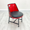 Esszimmer Stuhl aus Oelfass in Rot mit gesprayten Backsteinen auf der Rückseite, mit schwarzem Sitzpolster und schwarzen Metallbeinen auf weißem Holzboden vor weißem Hintergrund