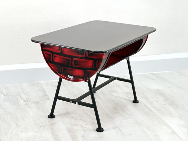 Oelfass Esszimmer Tisch in Rot mit aufgesprayten Backsteinen, schwarzer Granittischplatte und schwarzen Metallbeinen auf weißem Holzboden vor weißem Hintergrund