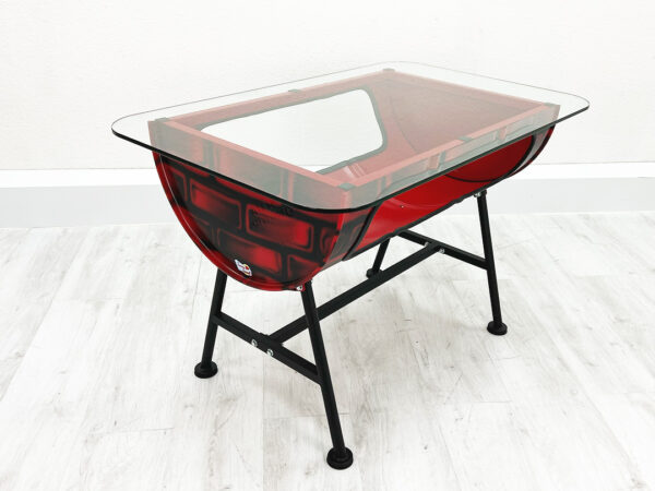 Roter Upcycling Oelfass Tisch mit Stauraum im Inneren und außen aufgesprayten Backsteinen mit Glastischplatte vor weißer Wand auf weißem Holzboden