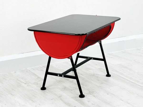 Roter Upcycling Oelfass Tisch mit Stauraum im Inneren und schwarzer Granittischplatte auf Metallfueßen vor weißer Wand auf weißem Holzboden