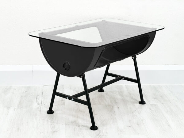 Uni schwarzer Oelfass Tisch mit Stauraum im Inneren und Glastischplatte auf schwarzen Metallfueßen vor weißer Wand auf weißem Holzboden