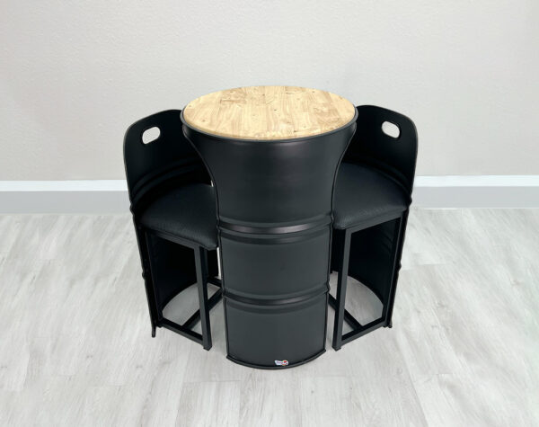 Schwarzer Stehtisch aus Oelfass in den seitlich 2 schwarzen Fass Stuehlen geschoben werden können mit heller Holztischplatte auf weißem Holzboden vor weißer Wand