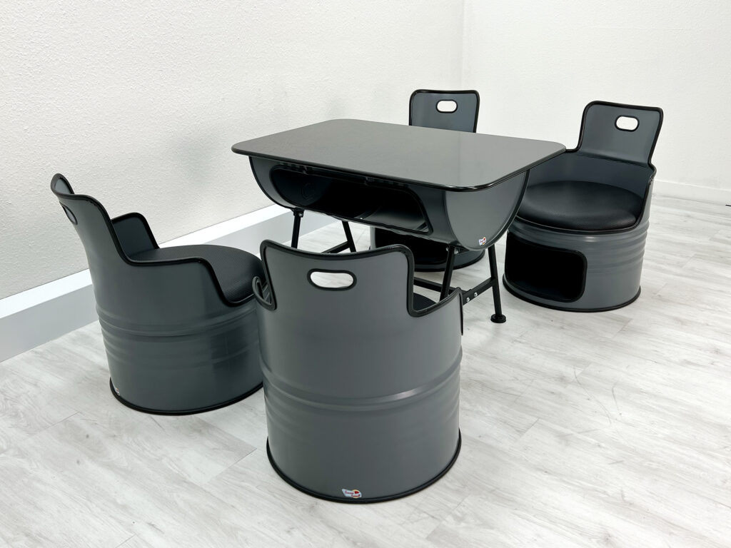 Ölfass Sitzgruppe in Grau mit schwarzen Sitzpolstern, bestehend aus vier Sesseln und einem Tisch mit Granitplatte auf weißem Holzboden.
